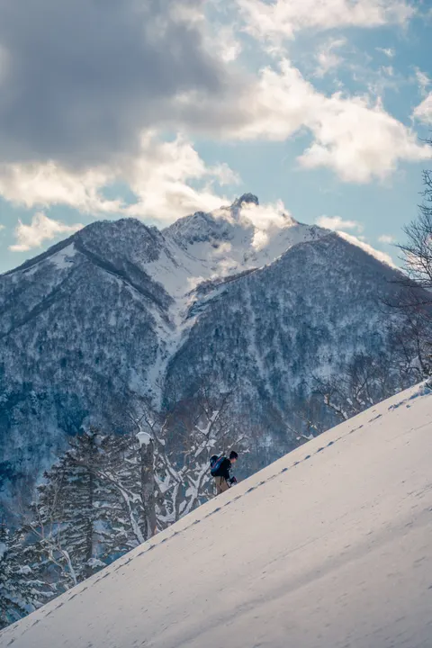 Skier on a steep backcountry slope below rocky peaks