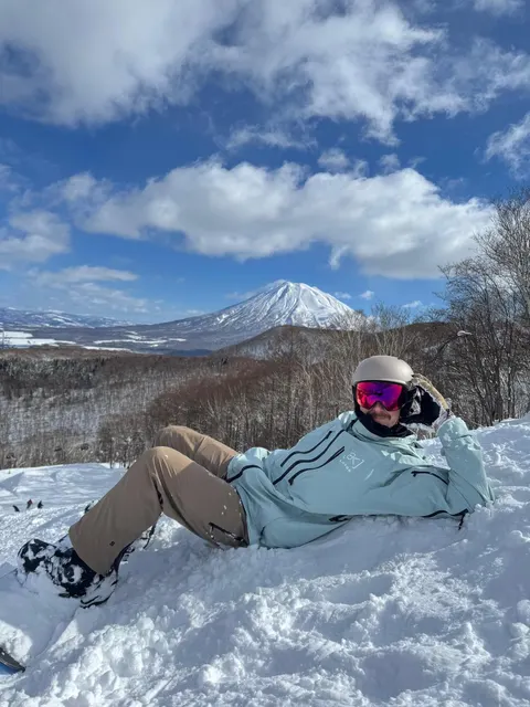 Snowboarder relaxing in the snow on a sunny day with Mt Yotei behind