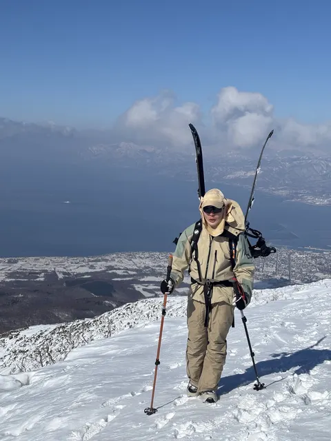 Skier carrying skis up a ridge above the sea