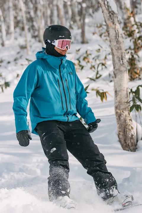 Snowboarder in a blue jacket in deep powder between trees