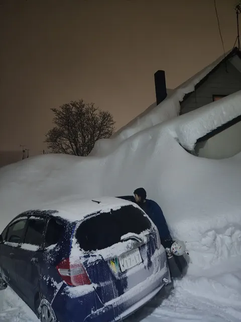 Car buried in snow at night outside the house