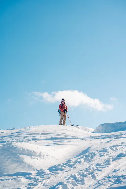 Skier standing on a snowy summit under a blue sky