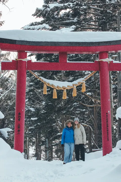 Two friends under a red torii gate in the snow