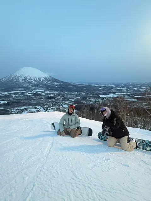 Two snowboarders sitting on a slope with Mt Yotei in the distance