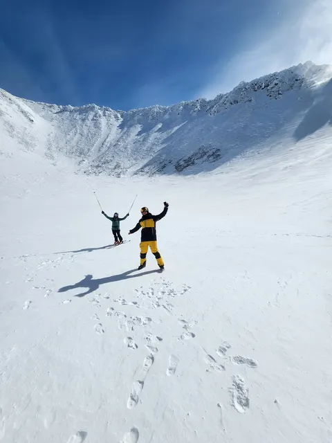Two skiers cheering in a snowy summit bowl